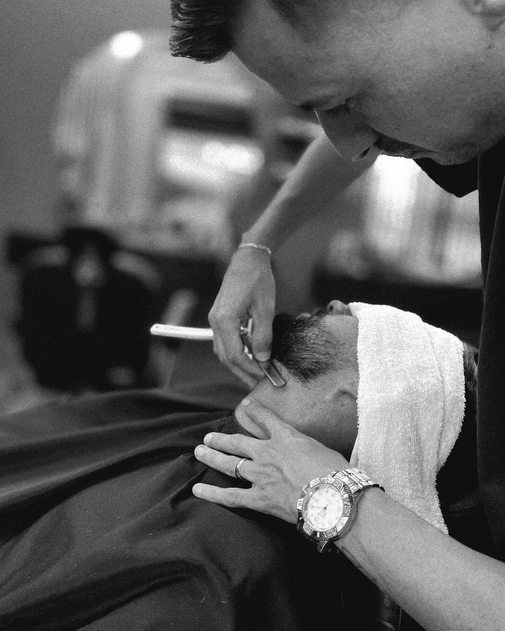 Barbeiro fazendo a barba de cliente com navalha e toalha