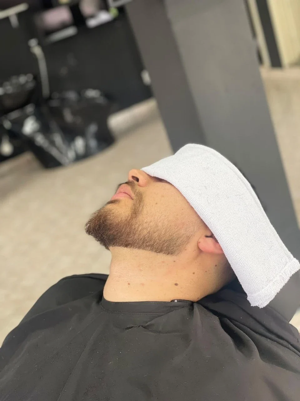 Cliente relaxando com toalha quente na cadeira da Navalha Barbearia